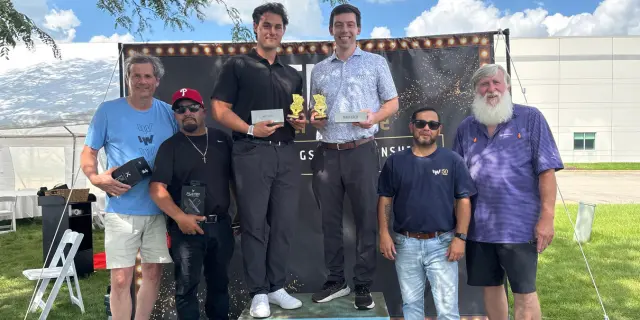 IW Technologies Bags Champions, Crowned Bags tournament winners hold their trophies on stage at IW Technologies Employee Appreciation Week.